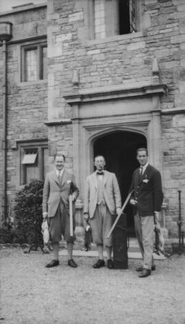 [A J Sylvester and two other men with shotguns outside a large house]